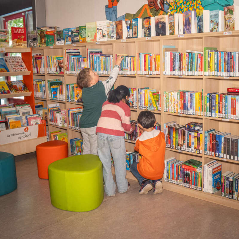 Drie leerlingen kiezen samen boeken uit het rek in de schoolbibliotheek