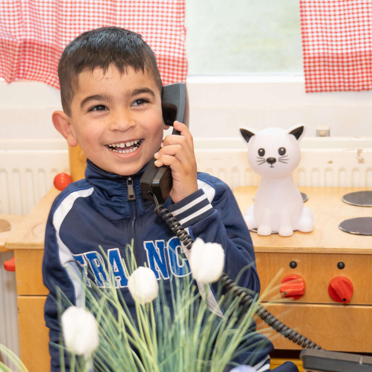 Lachende leerling van De Regenboog speelt met een telefoon in de klas