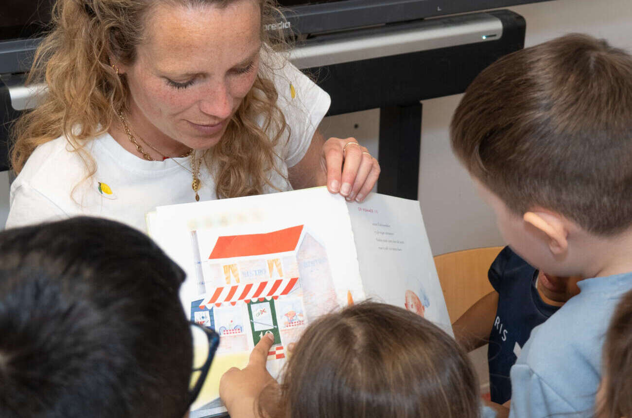 Leerkracht leest voor uit een prentenboek aan een groep aandachtige kleuters