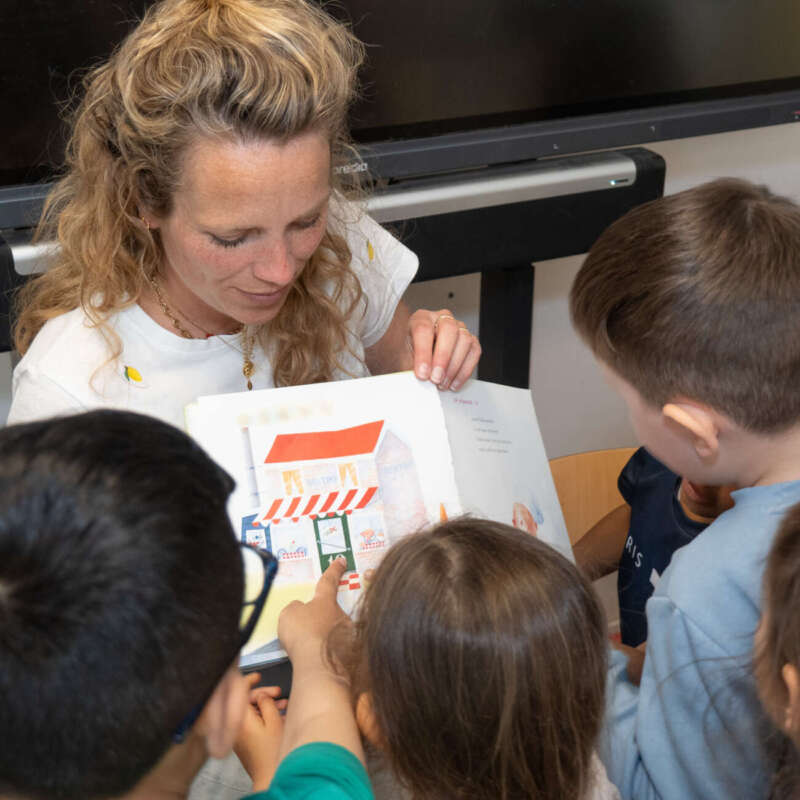 Leerkracht leest voor uit een prentenboek aan een groep aandachtige kleuters