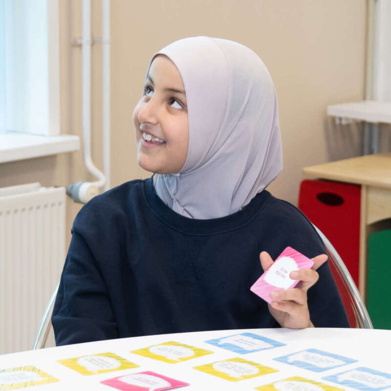 Lachend meisje met hoofddoek werkt aan tafel met kleurige woordkaartjes