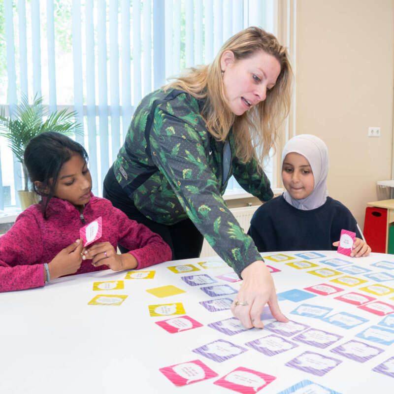Leerkracht legt twee leerlingen iets uit bij een opdracht met gekleurde taalkaartjes