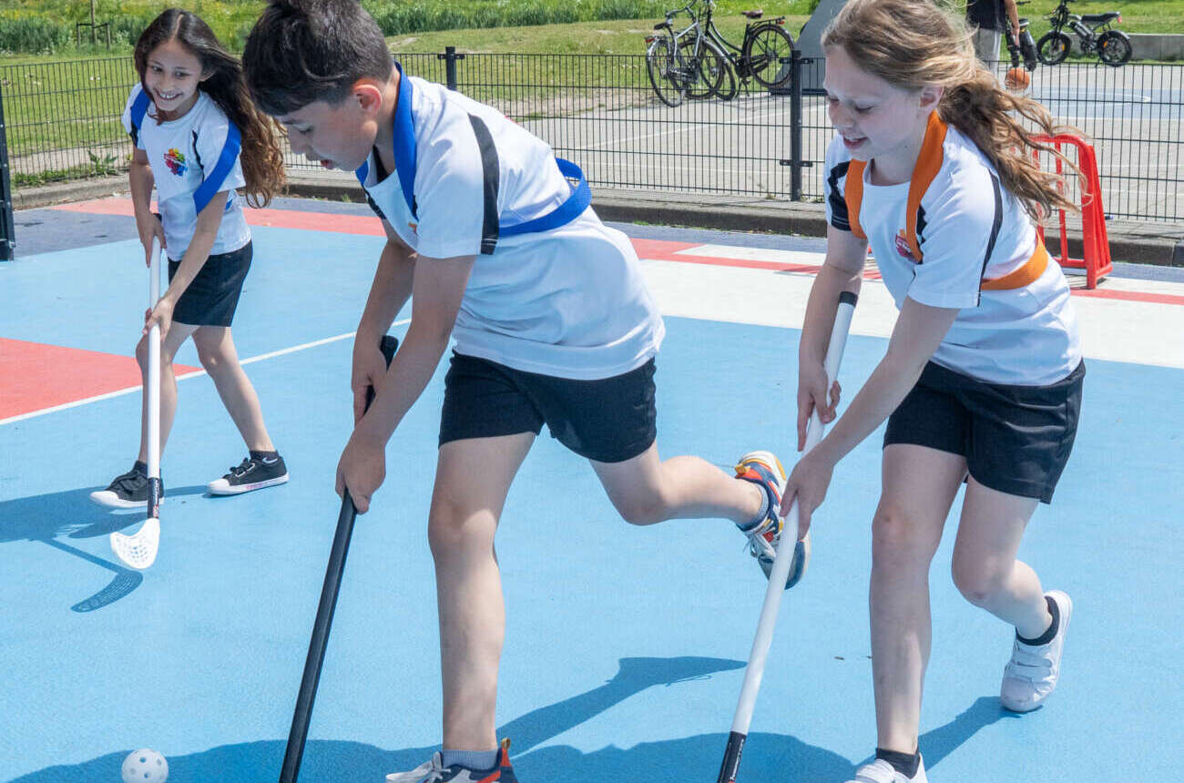 Drie leerlingen spelen unihockey op het blauw-rode sportveld bij de school