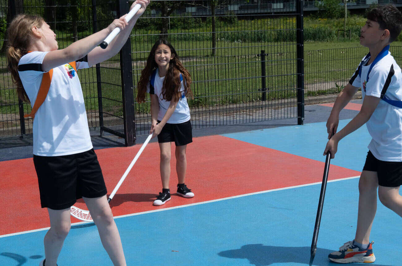 Drie enthousiaste leerlingen spelen unihockey in de buitensportkooi van De Regenboog