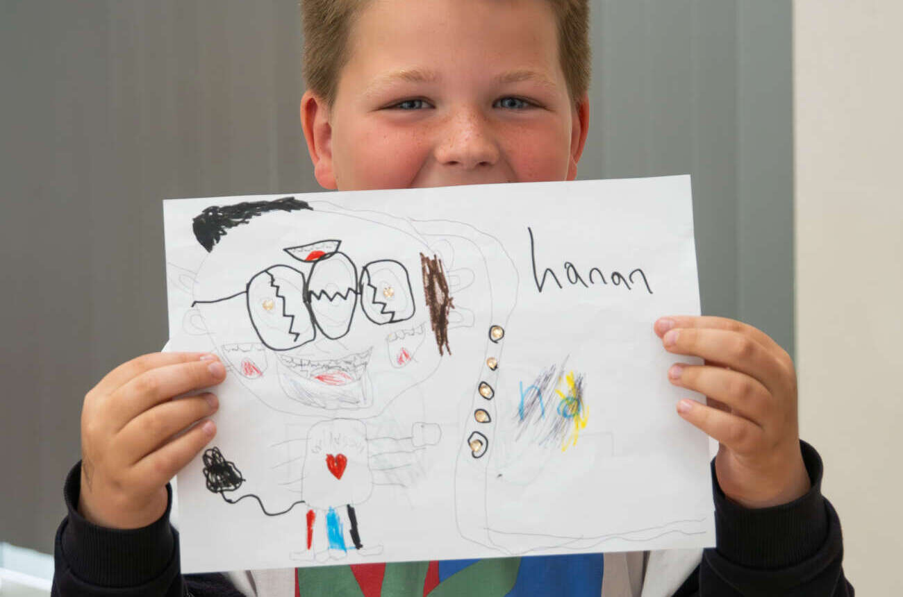 Lachende leerling laat trots zijn zelfgemaakte tekening met zijn naam zien