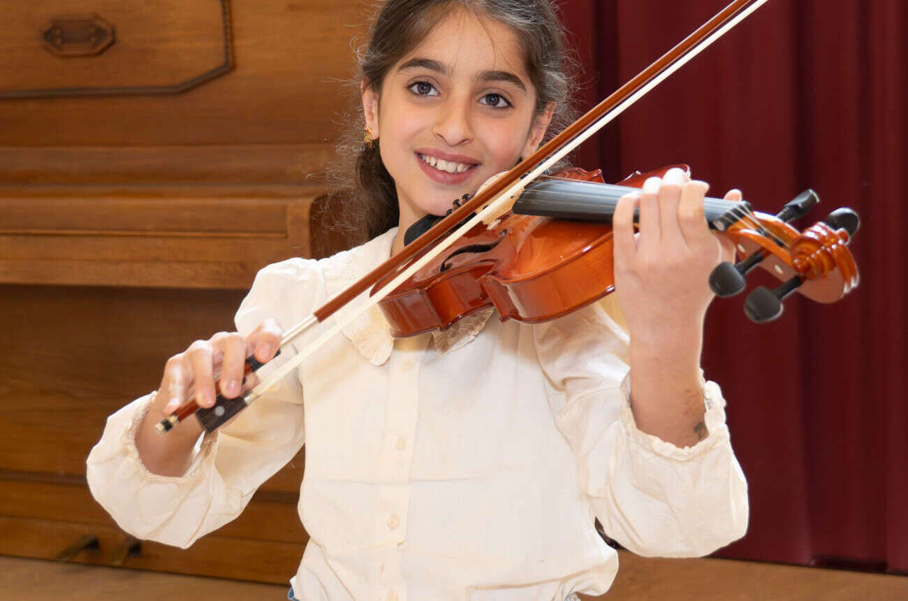 Leerling speelt enthousiast viool op het podium van de schoolaula