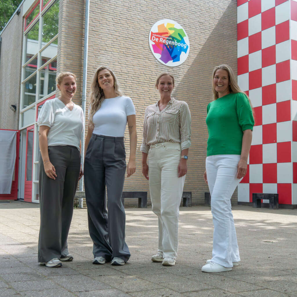 Vier teamleden van De Regenboog poseren samen voor de hoofdingang van de school
